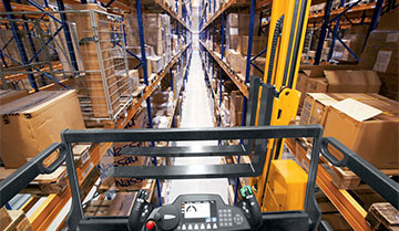 First-person view atop a Jungheinrich turret truck looking down warehouse aisle