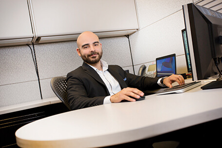 MCFA employee in suit sitting at office desk with computers