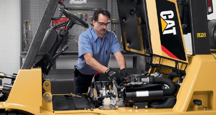 Worker in blue outfit and gloves working on a cat lift trucks's engine