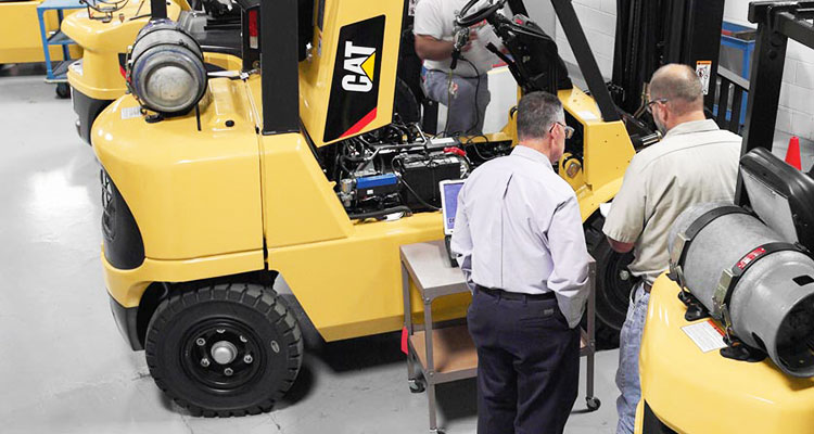 3 Cat forklifts in a row with workers inspecting them