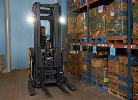 Operator in Cat pantograph reach truck positioned next to shelf of boxes