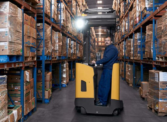 Side view of worker standing in Cat pantograph reach truck with light on