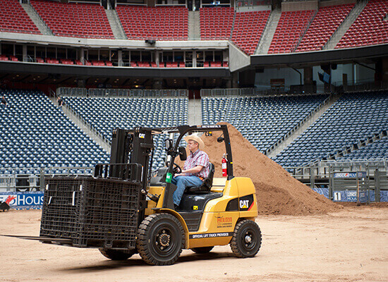 Operator Driving a Crate with a Cat Forklift Actross the Rodeo Stadium