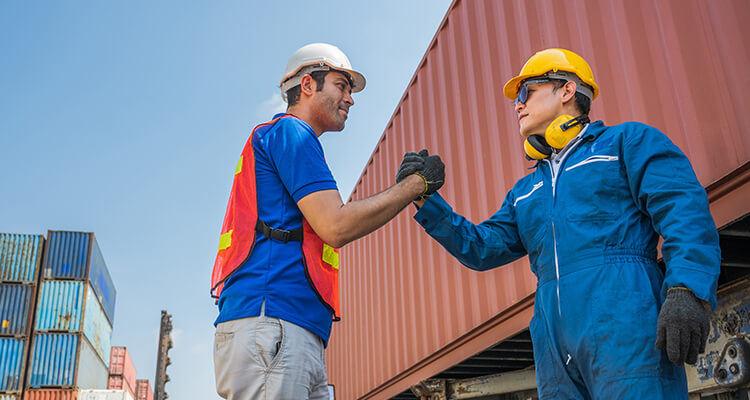 two co-workers shaking hands near shipping container